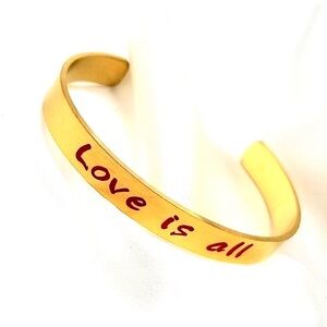 gold-tone or gold-plated cuff bracelet with the message "Love is all"